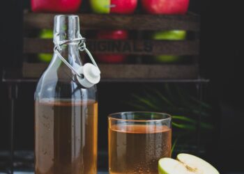 a glass bottle with brown liquid beside a glass of cold drink