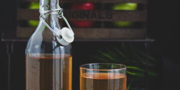 a glass bottle with brown liquid beside a glass of cold drink