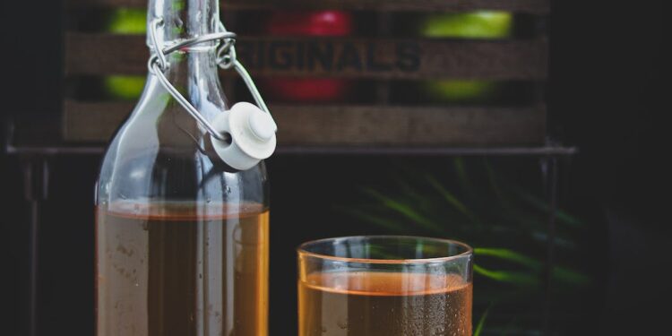 a glass bottle with brown liquid beside a glass of cold drink