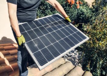 a person in black shirt holding a solar panel while standing on the roof