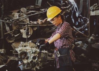 woman wears yellow hard hat holding vehicle part