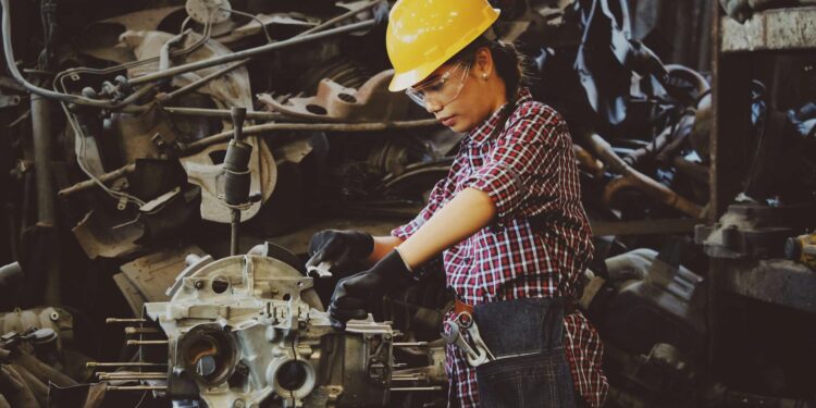 woman wears yellow hard hat holding vehicle part
