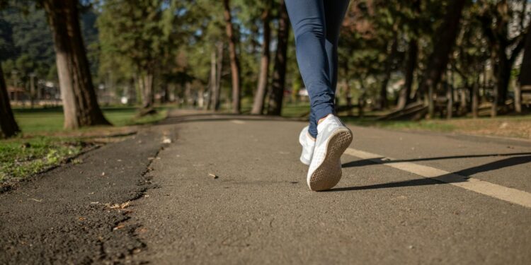 person in blue denim jeans and white sneakers walking on road