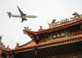 passenger airplane flying over a traditional chinese building
