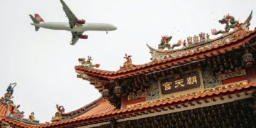 passenger airplane flying over a traditional chinese building