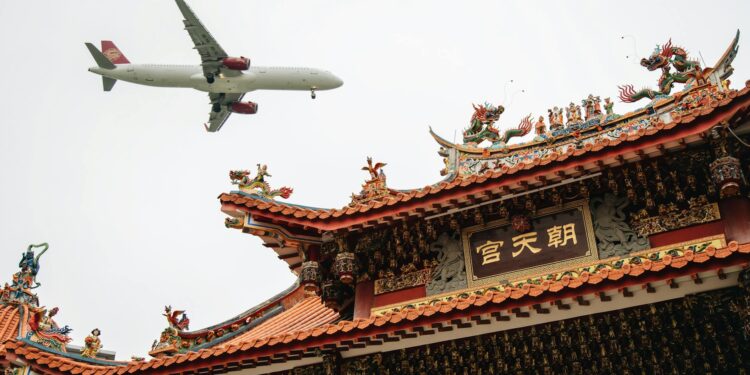 passenger airplane flying over a traditional chinese building