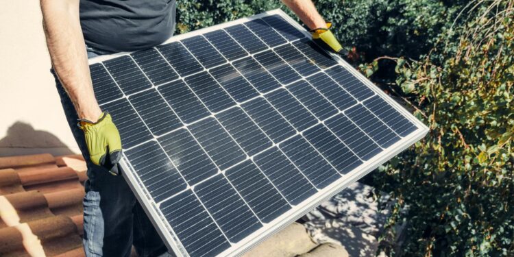 a person in black shirt holding a solar panel while standing on the roof