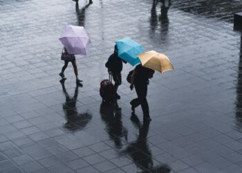 selective color photography of three person holding umbrellas under the rain