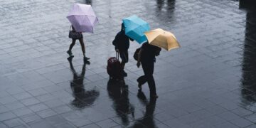 selective color photography of three person holding umbrellas under the rain
