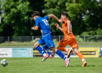 man in blue and orange jersey shirt running on green grass field during daytime